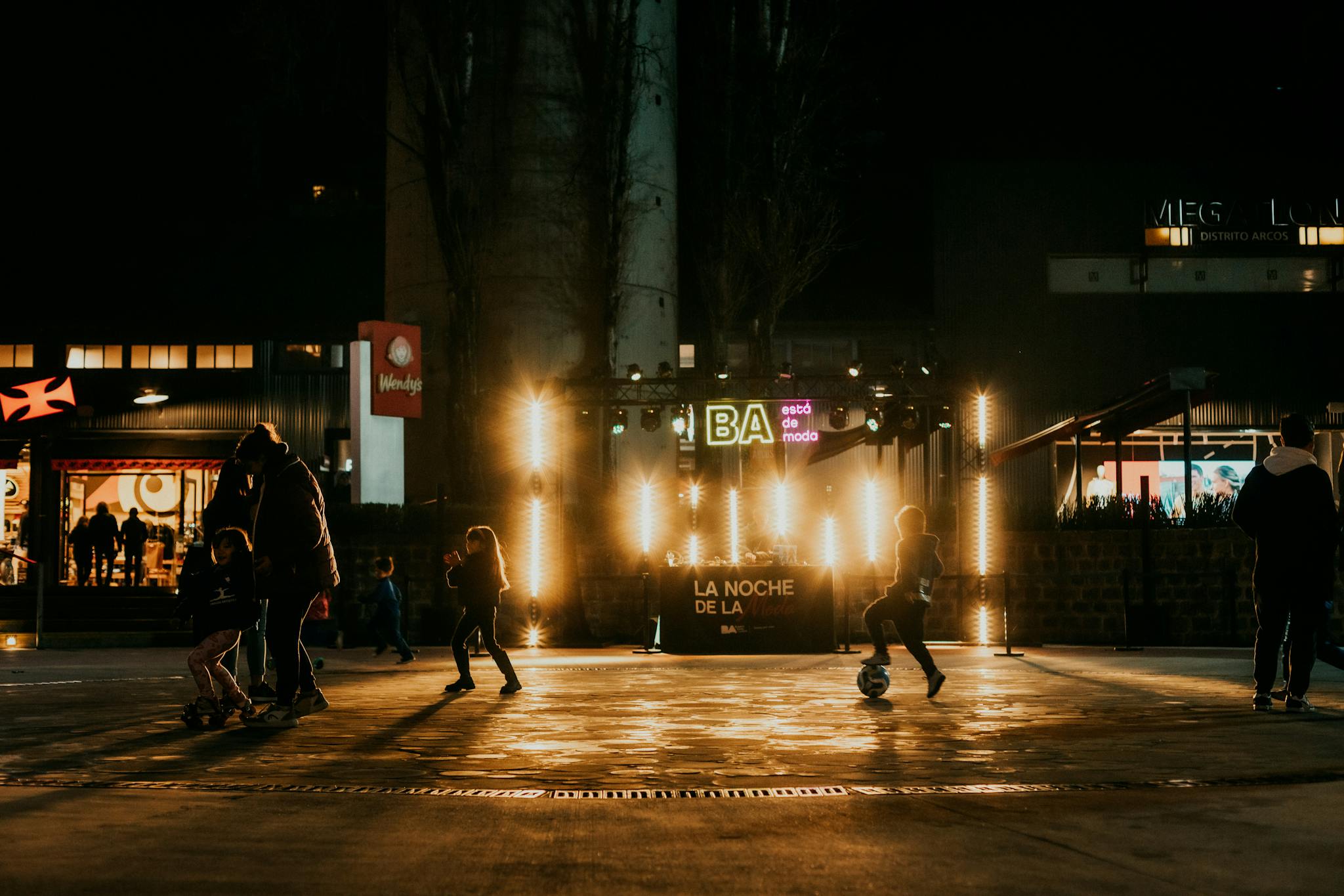 Children playing soccer at night in a vibrant urban setting with glowing street lights.